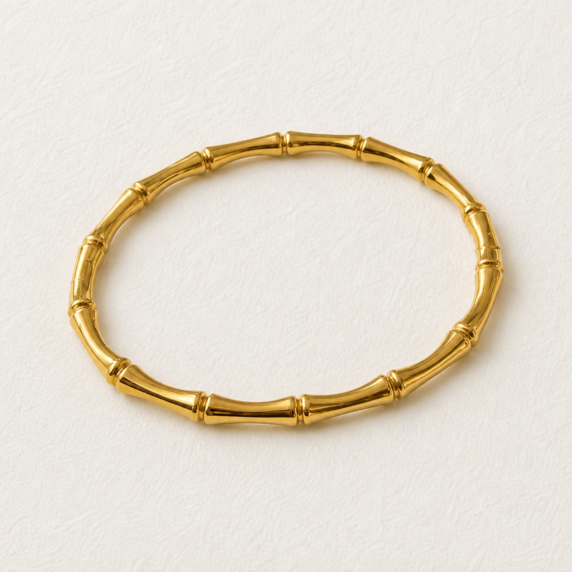 A gold-colored bamboo link bracelet on a textured off-white background.