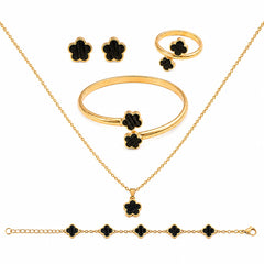 Gold jewelry set with black clover-shaped accents, including a necklace, bracelet, ring, and earrings, arranged on a white background.