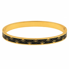 A gold-plated bangle bracelet featuring a black enamel inlay patterned with small gold eyes and radiating lines, shown against a plain white background.