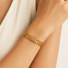 A gold leaf-patterned cuff bracelet with a central diamond cluster, shown worn on a person's wrist.