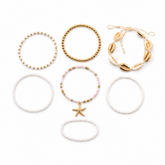 Six elastic beaded bracelets arranged on a plain white background, including gold bead loops, a white pearl-style bracelet with a gold starfish charm, a pink-and-gold beaded bracelet, and a white shell-bead bracelet.