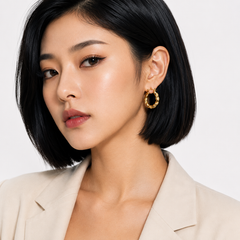 A close-up of a woman with a short black bob hairstyle wearing a textured gold hoop earring, paired with a light beige blazer against a clean white background.