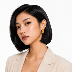 A woman with a short black bob hairstyle wearing a beige blazer and a gold hoop earring, photographed against a clean white background.