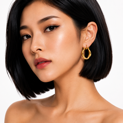 A close-up of a woman with a short black bob hairstyle wearing a gold hoop earring, set against a clean white background.