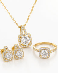 Gold jewelry set featuring a pendant necklace, matching stud earrings, and a ring, each with a square halo design set with clear gemstones on a white background.