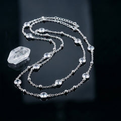 A silver-toned chain necklace with multiple clear faceted gemstones and a larger clear crystal pendant, displayed on a glossy black reflective surface.