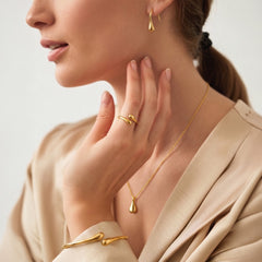 A close-up lifestyle shot of a woman wearing elegant gold jewelry, including a teardrop pendant necklace, a matching teardrop hoop earring, and a gold ring and bracelet with a twisted branch-like design.