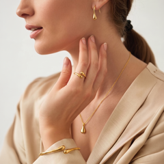 A close-up lifestyle shot of a woman wearing elegant gold jewelry, including a teardrop pendant necklace, a matching teardrop hoop earring, and a gold ring and bracelet with a twisted branch-like design.