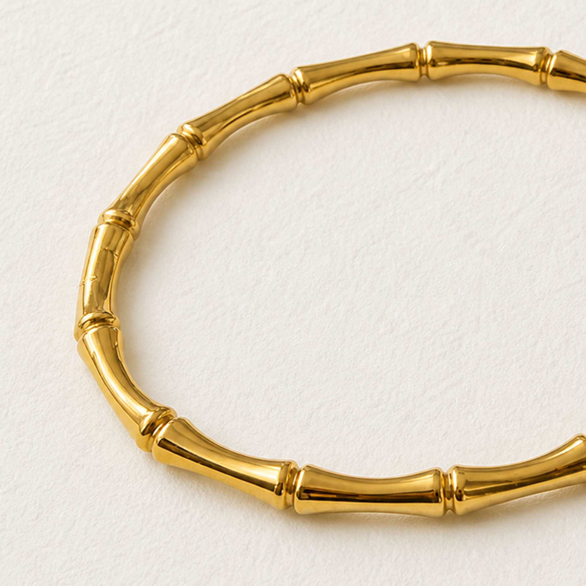 A gold-toned bangle bracelet designed to look like a segmented bamboo stalk, photographed on a textured off-white background.