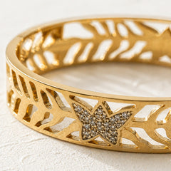 A close-up of a gold bangle bracelet featuring a star-shaped pavé diamond centerpiece and an intricate openwork filigree pattern.