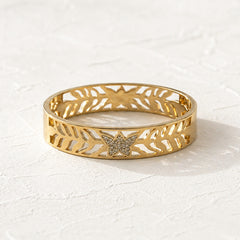 A gold bangle bracelet with a butterfly motif and openwork leaf patterns, set against a textured white background.