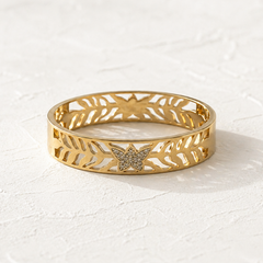 A gold bangle bracelet with a butterfly motif and openwork leaf patterns, set against a textured white background.