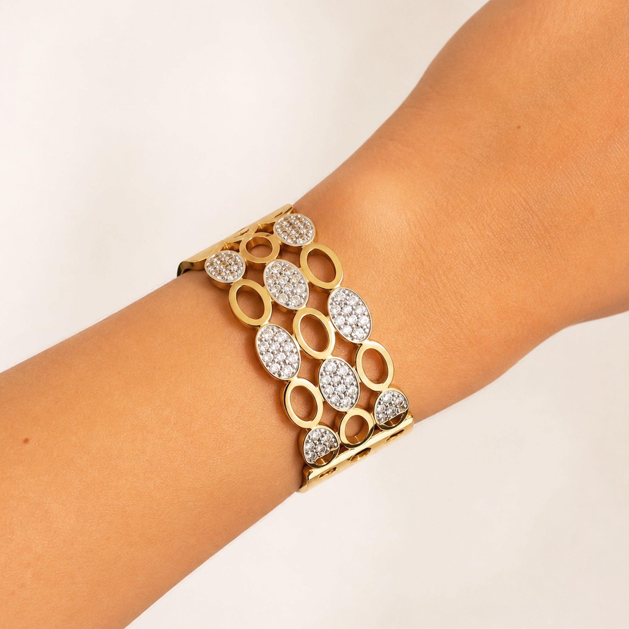 A gold cuff bracelet with pavé-set clear stones, shown worn on a person's wrist against a plain light background.