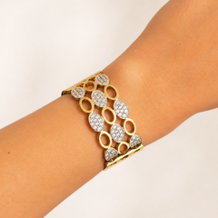 A gold cuff bracelet with pavé-set clear stones in oval and teardrop shapes, shown worn on a person's wrist against a plain light background.