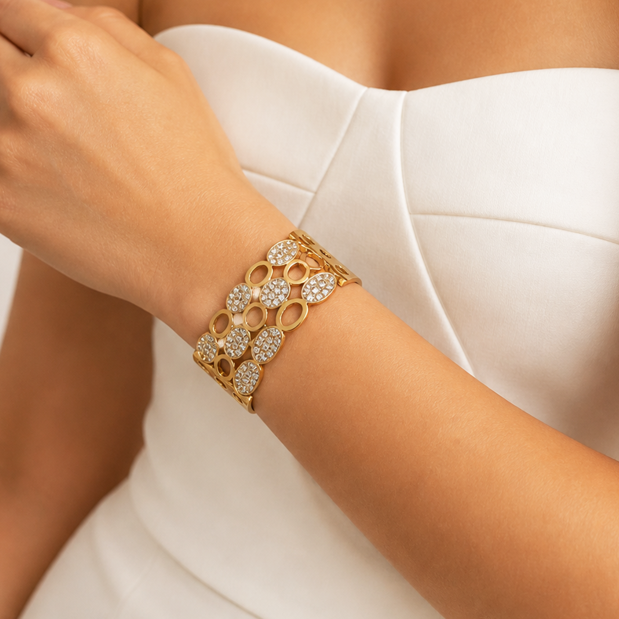 A close-up of a woman's wrist wearing a gold cuff bracelet adorned with pavé-set diamonds and central round diamonds, styled with a white strapless dress.