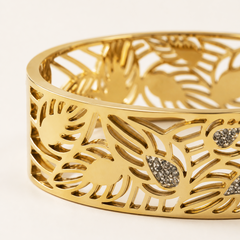 Gold-toned openwork cuff bracelet with a cutout leaf pattern and small pavé-set clear stones, photographed on a clean white background.