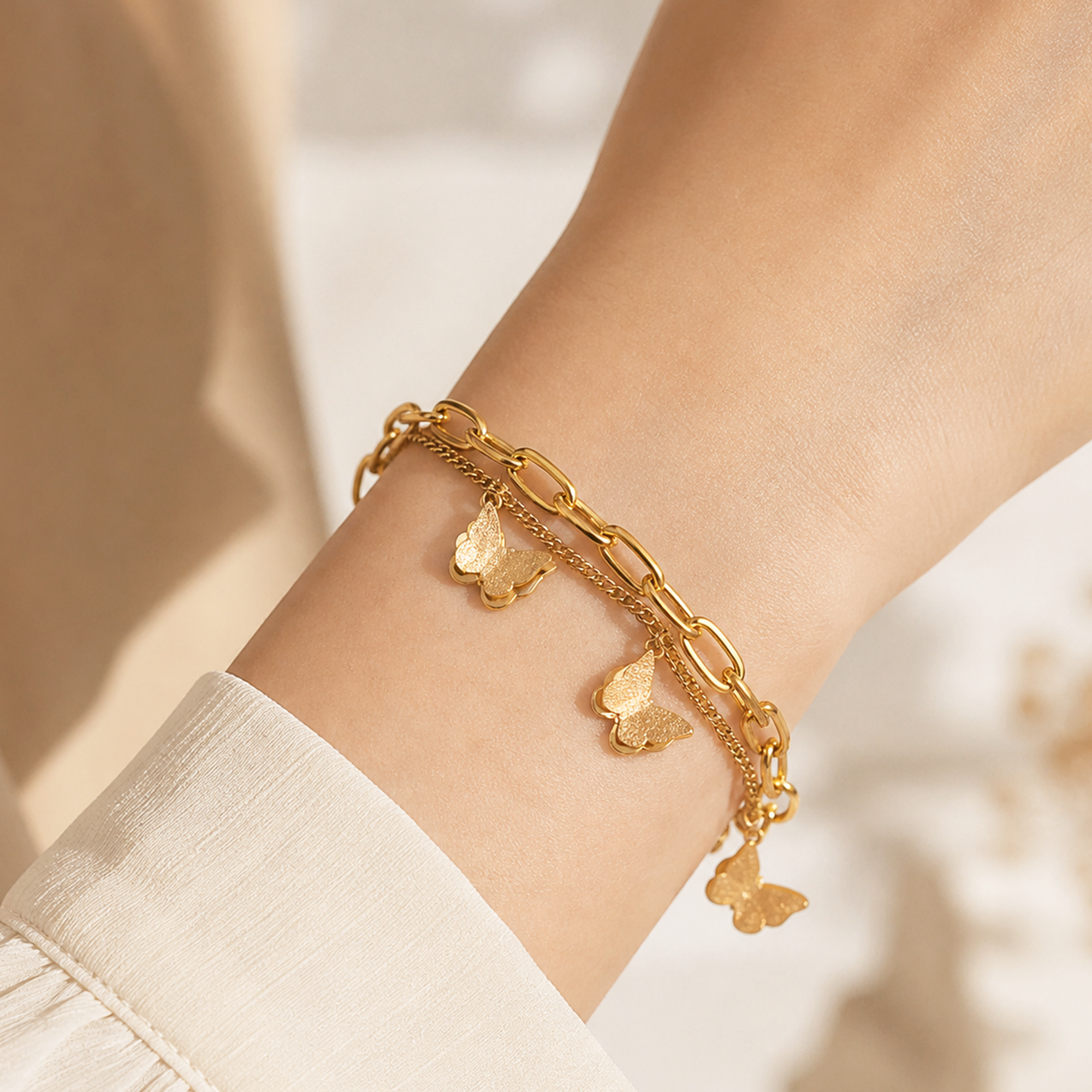 A close-up of a delicate gold chain bracelet with butterfly charms worn on a person's wrist, paired with a white sleeve.