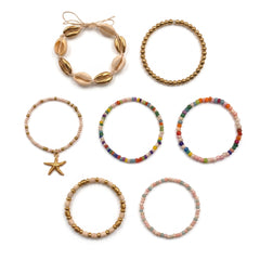 Seven beaded bracelets and one shell bracelet arranged on a plain white background. The bracelets include gold-toned beads, pastel pink and blue beads, rainbow-colored beads, and natural beige shells with a starfish charm.