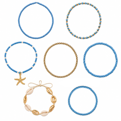 Seven beaded bracelets arranged on a plain white background, including blue bead strands with gold starfish, blue and gold bead accents, a gold chain bracelet, and a bracelet with white shell-like beads and gold details.