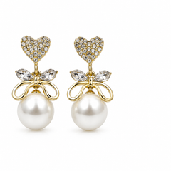 A pair of gold drop earrings featuring a heart-shaped cluster of clear pavé stones, a bow-shaped setting with marquise-cut clear stones, and a large white pearl dangling below, shown on a plain white background.