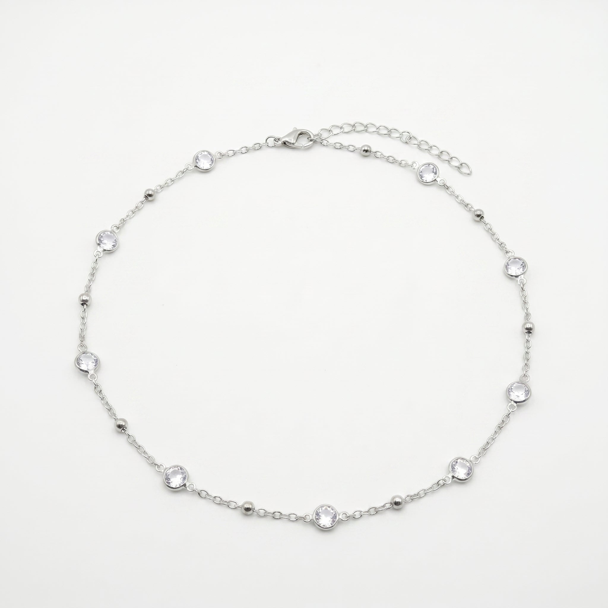 A delicate silver chain anklet featuring seven small, clear round-cut gemstones spaced evenly along the chain, displayed on a clean white background.