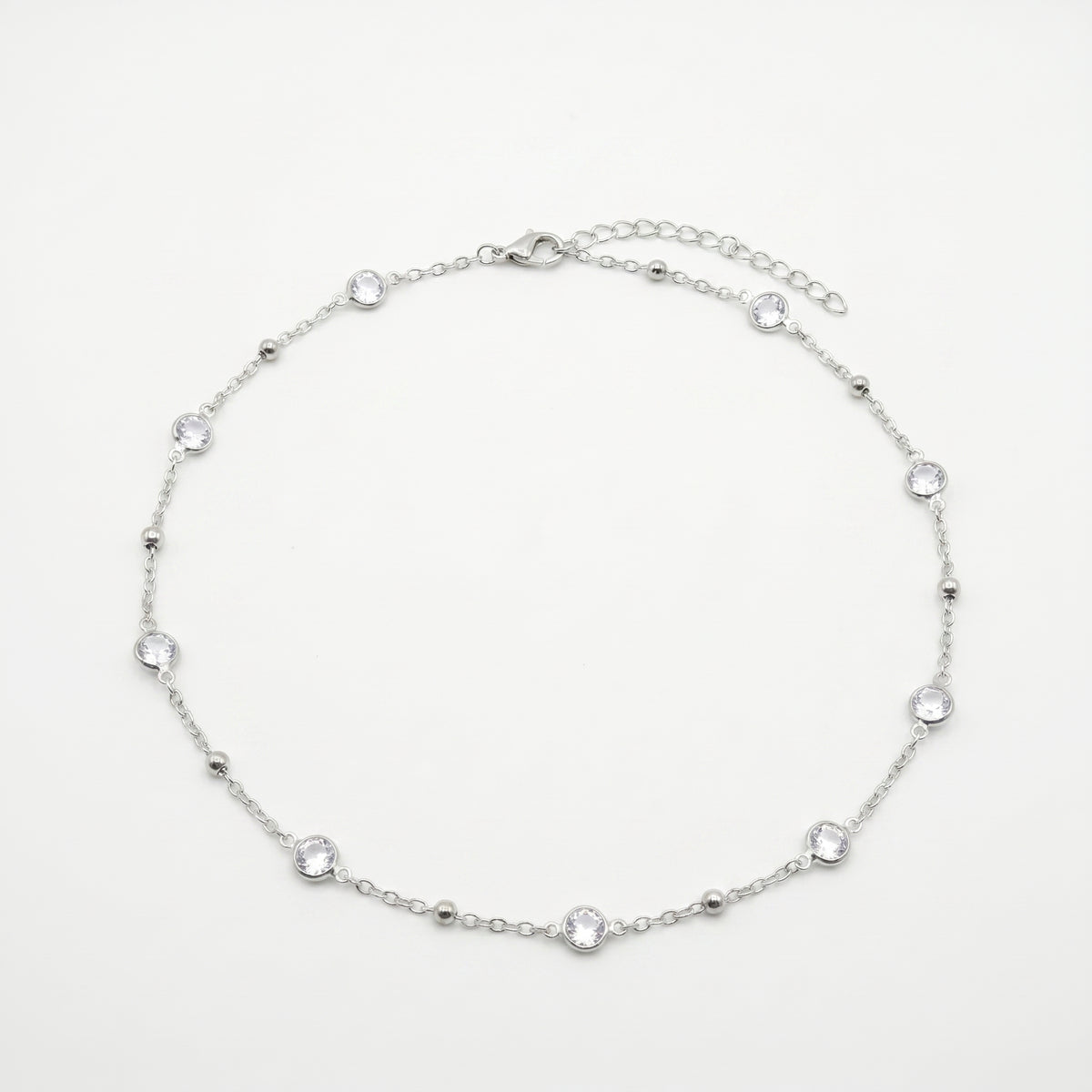 A delicate silver chain anklet featuring seven small, clear round-cut gemstones spaced evenly along the chain, displayed on a clean white background.