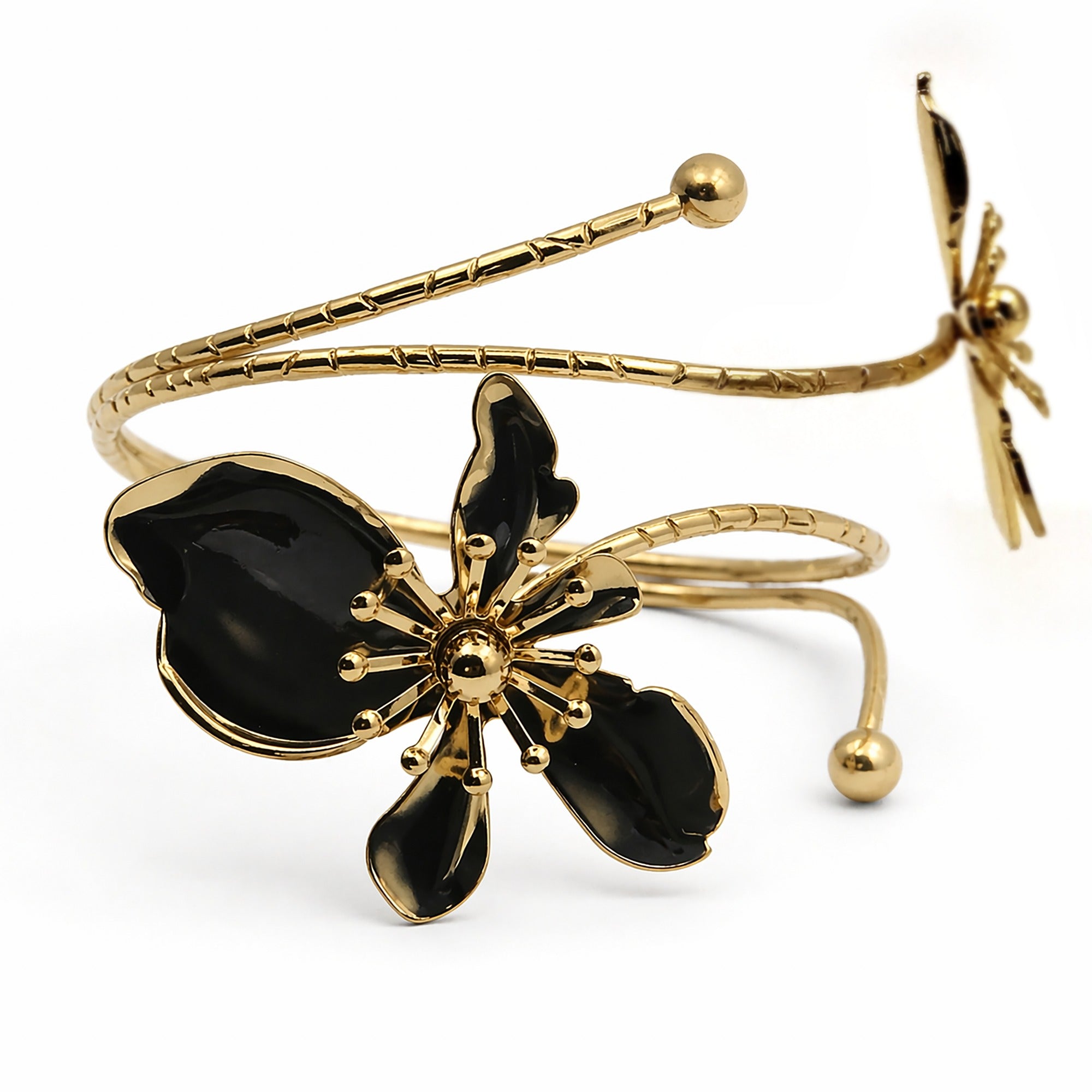 Gold-plated open cuff bracelet featuring a large black enamel flower on the front and a smaller matching flower on the back, set against a plain white background.