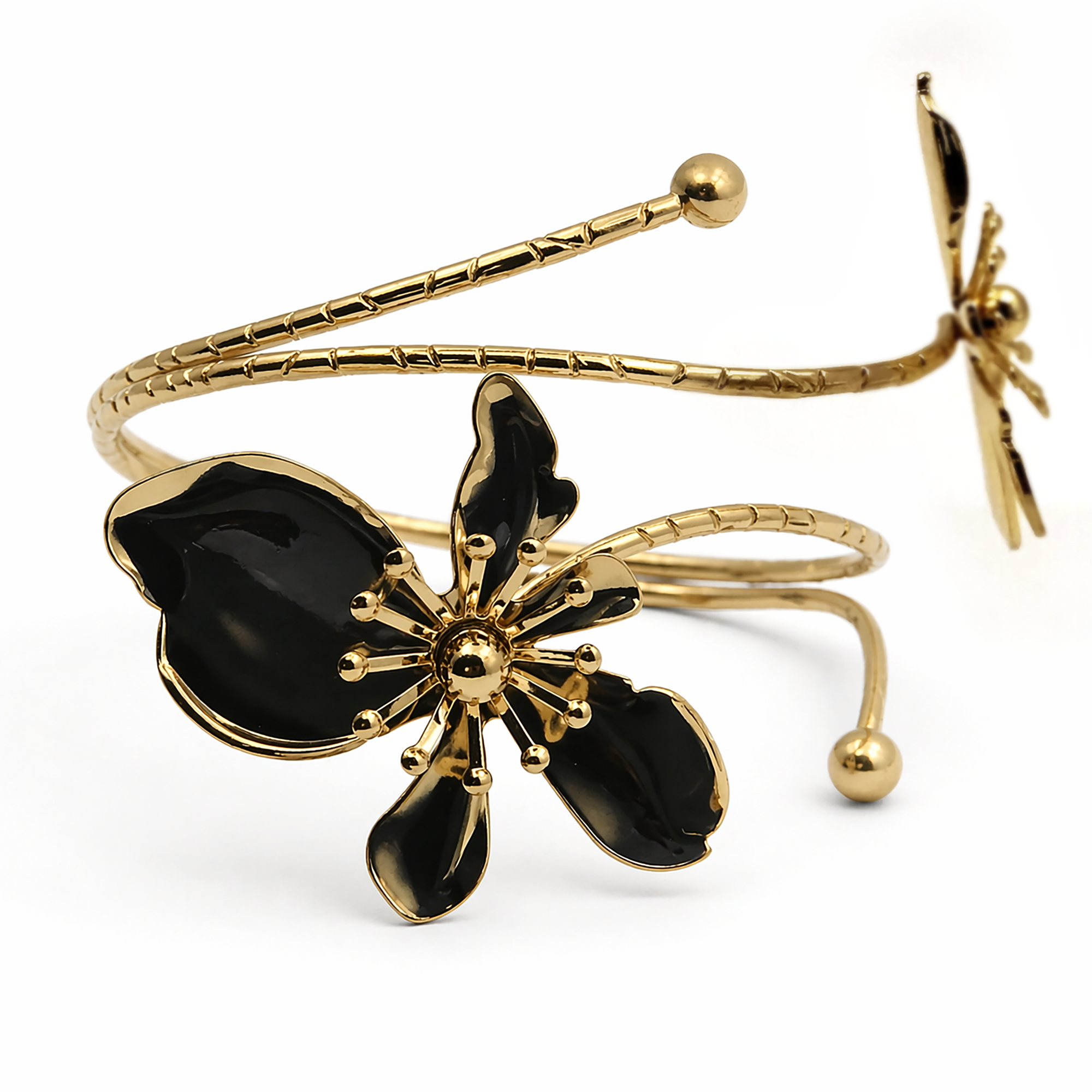 Gold-tone open cuff bracelet featuring a large glossy black flower and a smaller matching flower on the opposite side, photographed on a clean white background.