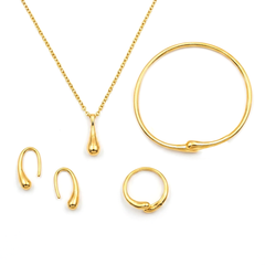Gold jewelry set featuring a teardrop pendant necklace on a delicate chain, a large open-ended hoop, a small ring, and two small hook-style earrings, all arranged on a plain white background.