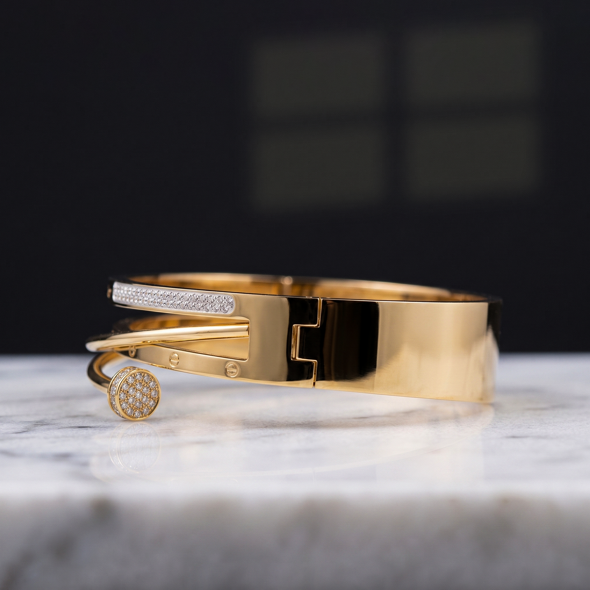 A polished gold-tone cuff bracelet with a pavé-set rectangular bar and a round pavé-set end, displayed on a white marble surface against a dark blurred background.