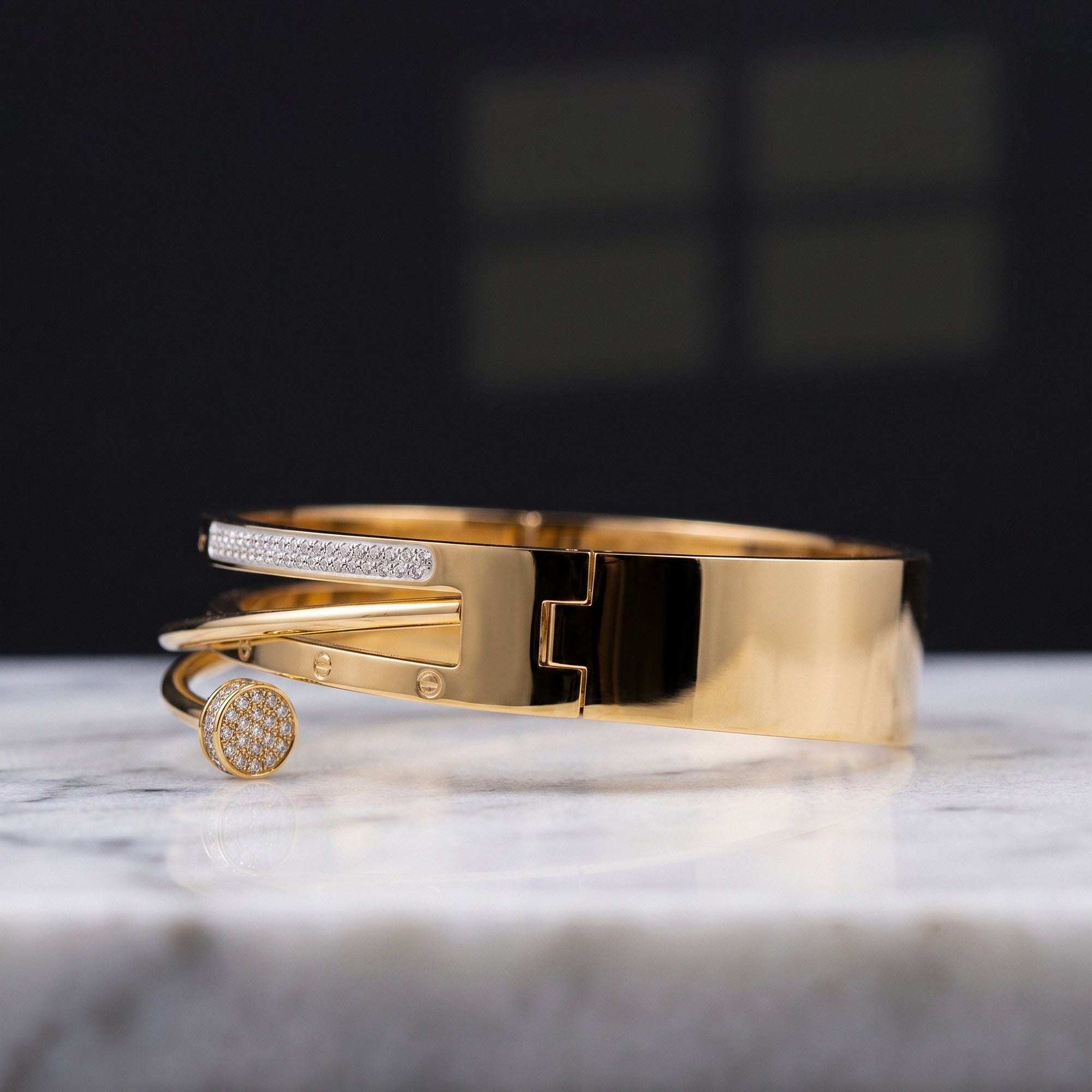 A polished gold bangle bracelet with a pavé-set round bezel charm, resting on a white marble surface against a dark, blurred background.